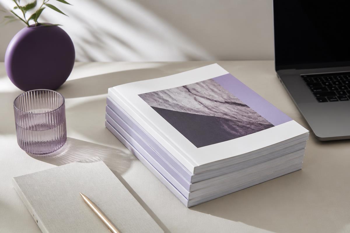 Stack of printed guides and a notebook beside a laptop on a pale desk